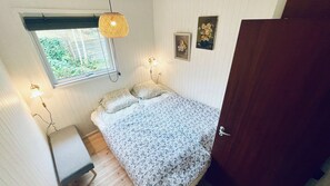 A bedroom with a bed, a window, a door, and a wall-mounted light fixture.