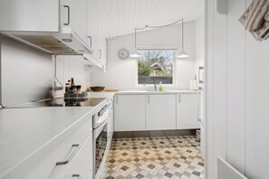A kitchen with white cabinets, a stove, a sink, and a window with a view of a house.