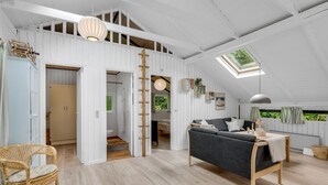 Un loft espacioso con techo alto, vigas de madera, una cama en entrepiso, un sofá, una mesa de comedor y una escalera.
