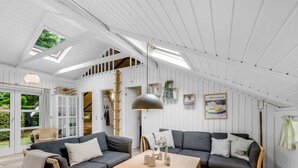 Un moderno loft con techo alto, tragaluces, un conjunto de sofás, una mesa de madera y una estantería.