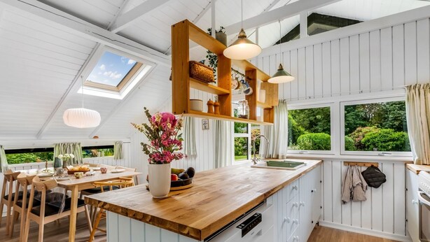 Una cocina moderna con encimeras de madera, una isla central, luces colgantes y vistas al exterior.