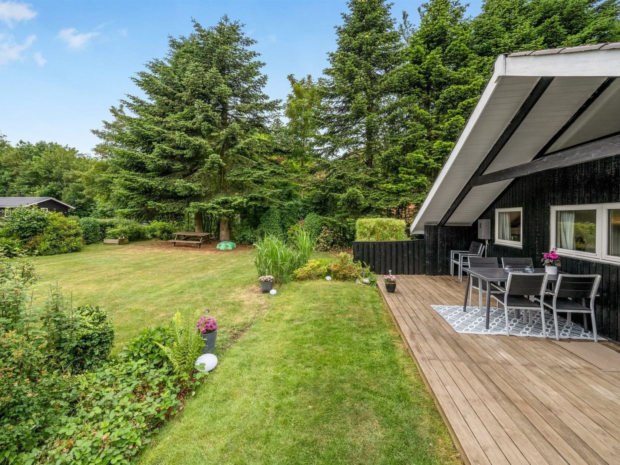 A wooden deck with outdoor furniture, a grassy yard, and a black building with windows.