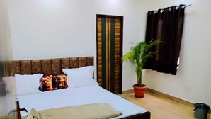 A bedroom with a bed, a potted plant, a door, and a window with curtains. - Matoshree Villa (Kotra)