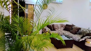 A living room with a sofa, a coffee table, and a large potted plant. - Matoshree Villa (Kotra)