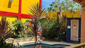 Un espace piscine avec un bâtiment jaune et rouge, une petite piscine et une porte bleue.