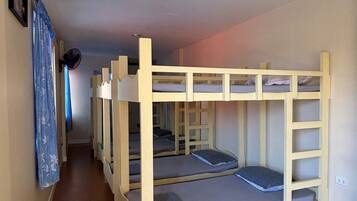 Habitación con literas, piso de madera, ventilador de techo y pasillo con cortina.
