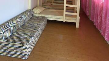 Habitación con literas, un sofá, suelo de madera y cortinas rosadas.