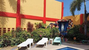 Un espace piscine avec des chaises longues, une fontaine décorative et un bâtiment à la façade rouge et jaune.