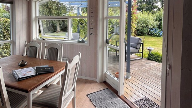 Ein Essbereich mit Holztisch und -stühlen, großen Fenstern und Blick auf einen Garten.