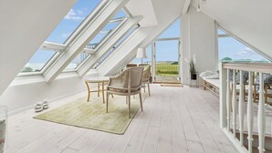 A spacious attic room with skylights, a wooden floor, a dining area with chairs, and a view of the outdoors. - Lovely cottage with amazing sea view (Assens)