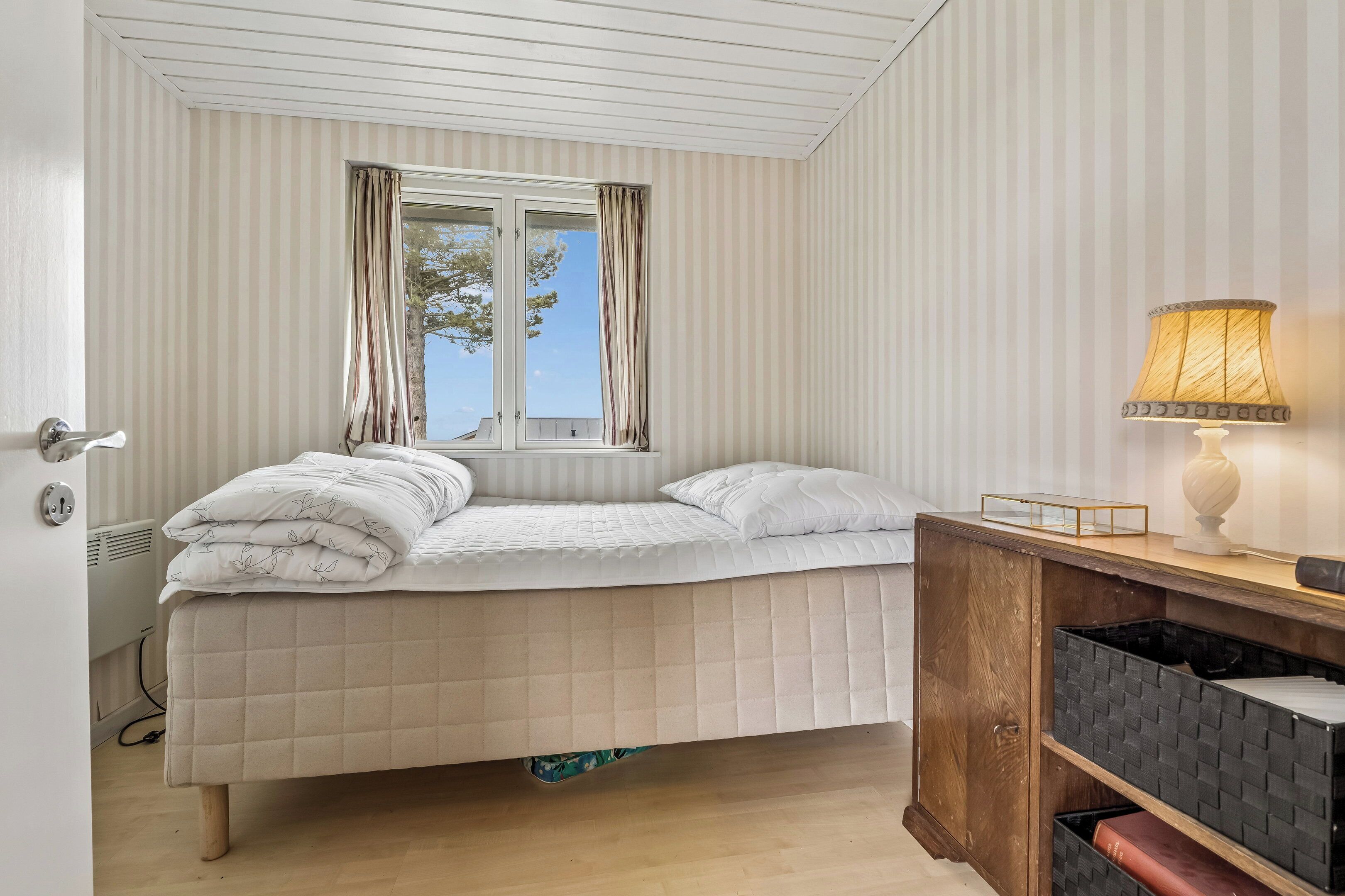 A bed with a window, a lamp, and a wooden cabinet.