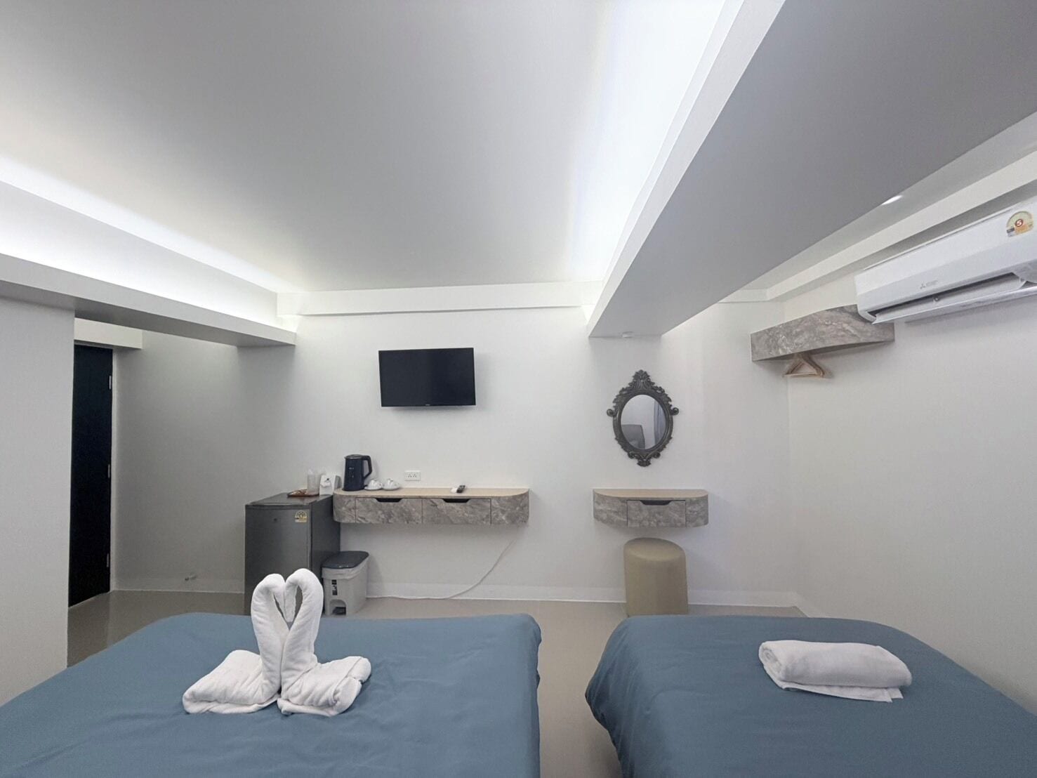 Una habitación de hotel moderna con dos camas, un televisor, un tocador de mármol y un equipo de aire acondicionado.