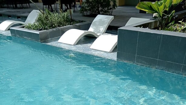A clear swimming pool with a modern design, including a white lounge chair and a planter with greenery.