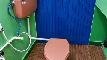 A restroom with a brown toilet, a blue partition, and a yellow bucket.