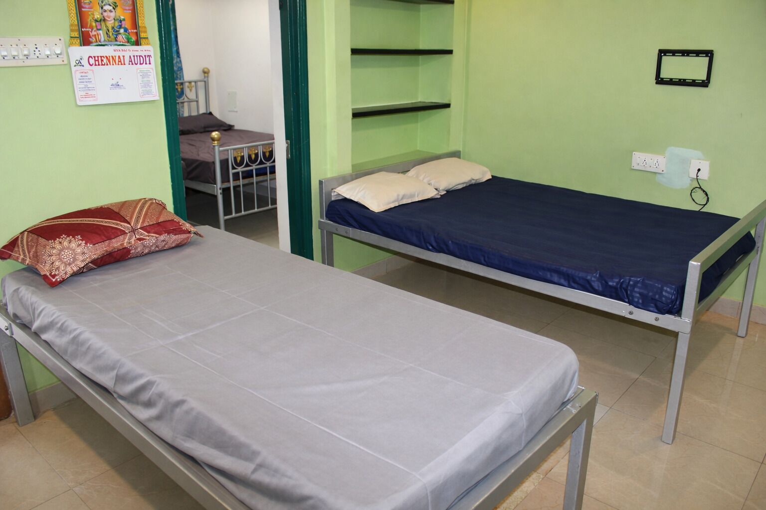 Una habitación con dos camas individuales, un escritorio, una silla y una pared verde con un cartel.