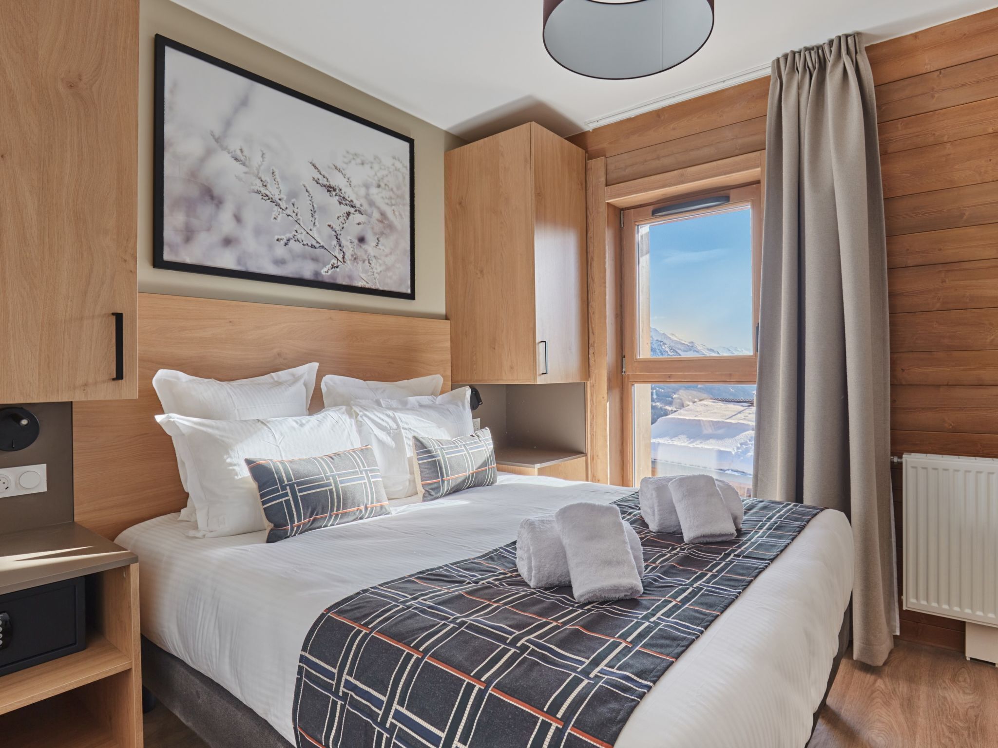 Une chambre d’hôtel moderne avec un grand lit, une vue sur un paysage enneigé, un lambris en bois et une œuvre d’art encadrée au mur.