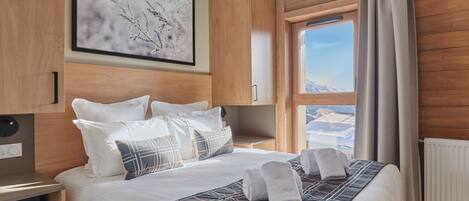 Une chambre d’hôtel moderne avec un grand lit, une vue sur un paysage enneigé, un lambris en bois et une œuvre d’art encadrée au mur.