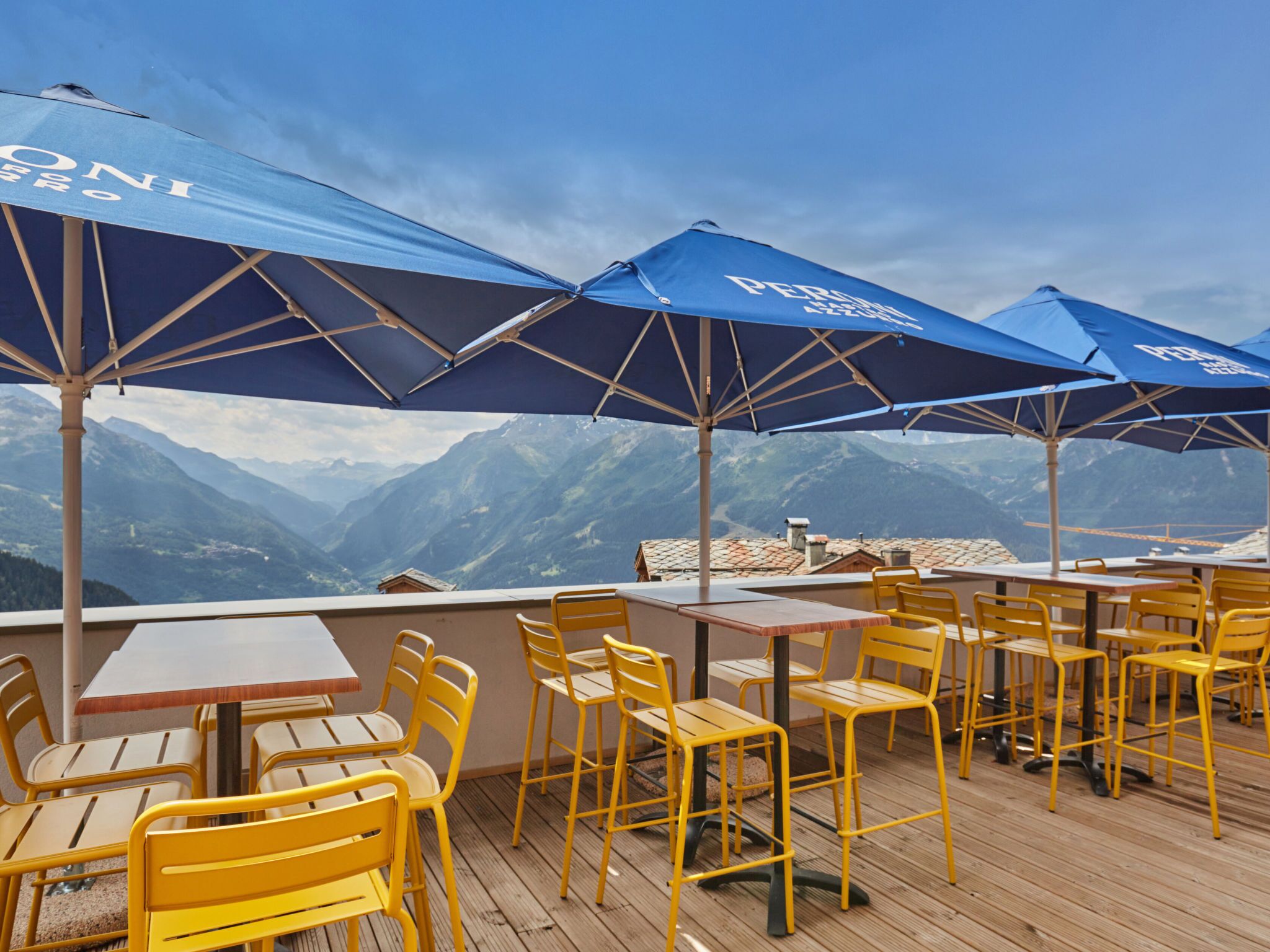 Outdoor seating with tables and chairs, blue umbrellas, and a mountainous backdrop.