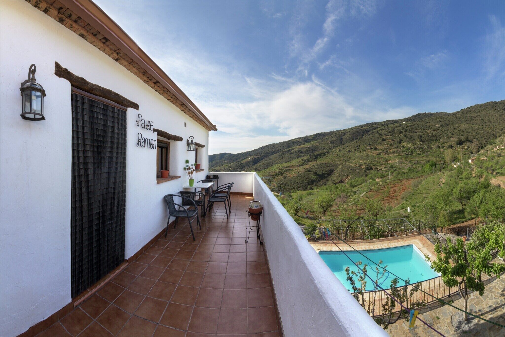 Un balcon avec une piscine, une table, des chaises et une vue sur un paysage vallonné.