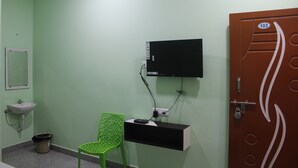 Habitació amb paret verda, un vàter blanc, cadira verda, televisió penjada a la paret i una porta amb un tancament.