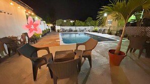 Un área de piscina al aire libre con sillones, una mesita y una flor decorativa.