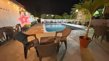 An outdoor pool area with lounge chairs, a small table, and a decorative flower.