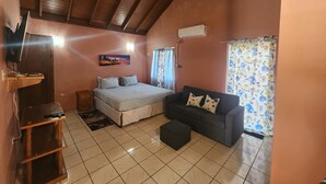 Un dormitorio con cama, sofá, televisión y ventana con cortinas.