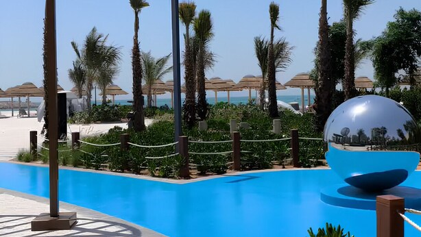 Area piscina con palme, una grande sfera riflettente e ombrelloni da spiaggia.