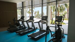 Una palestra con tapis roulant, ellittiche e vogatore, ampie finestre e pavimento blu.