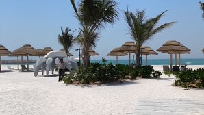 Un resort sulla spiaggia con ombrelloni in paglia, palme e una vista limpida sul mare.