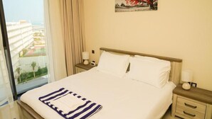 Una camera d'albergo con un letto, un comodino, una lampada, una finestra vista edifici e un quadro appeso al muro.