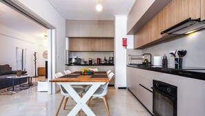 A modern kitchen with a dining area, featuring a wooden table, white chairs, and a variety of kitchen appliances. - Amphitryon Residence | 2BR Apartment in Glyfada (Glifada)