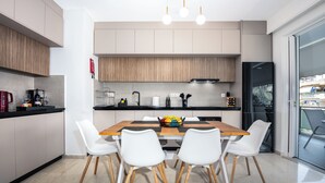 A modern kitchen with white cabinets, a wooden dining table, and white chairs. - Amphitryon Residence | 2BR Apartment in Glyfada (Glifada)
