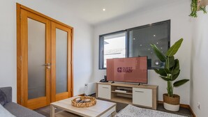 A modern living room with a wooden door, a television, a plant, and a sofa. - GuestReady-Charming Ponta Delgada Retreat (Ponta Delgada)