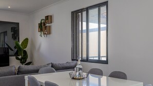 A modern dining area with a white table, grey chairs, a large window, and a plant on the wall. - GuestReady-Charming Ponta Delgada Retreat (Ponta Delgada)