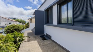 A modern building with a flat roof, large windows with blinds, and a concrete pathway. - GuestReady-Charming Ponta Delgada Retreat (Ponta Delgada)