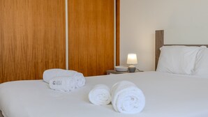 A hotel room with a bed, a nightstand with a lamp, and rolled towels on the bed. - GuestReady-Charming Ponta Delgada Retreat (Ponta Delgada)