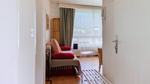 A room with a bed, a small table, a chair, a window with curtains, and a door. - Flüela Lounge by Interhome (Davos)