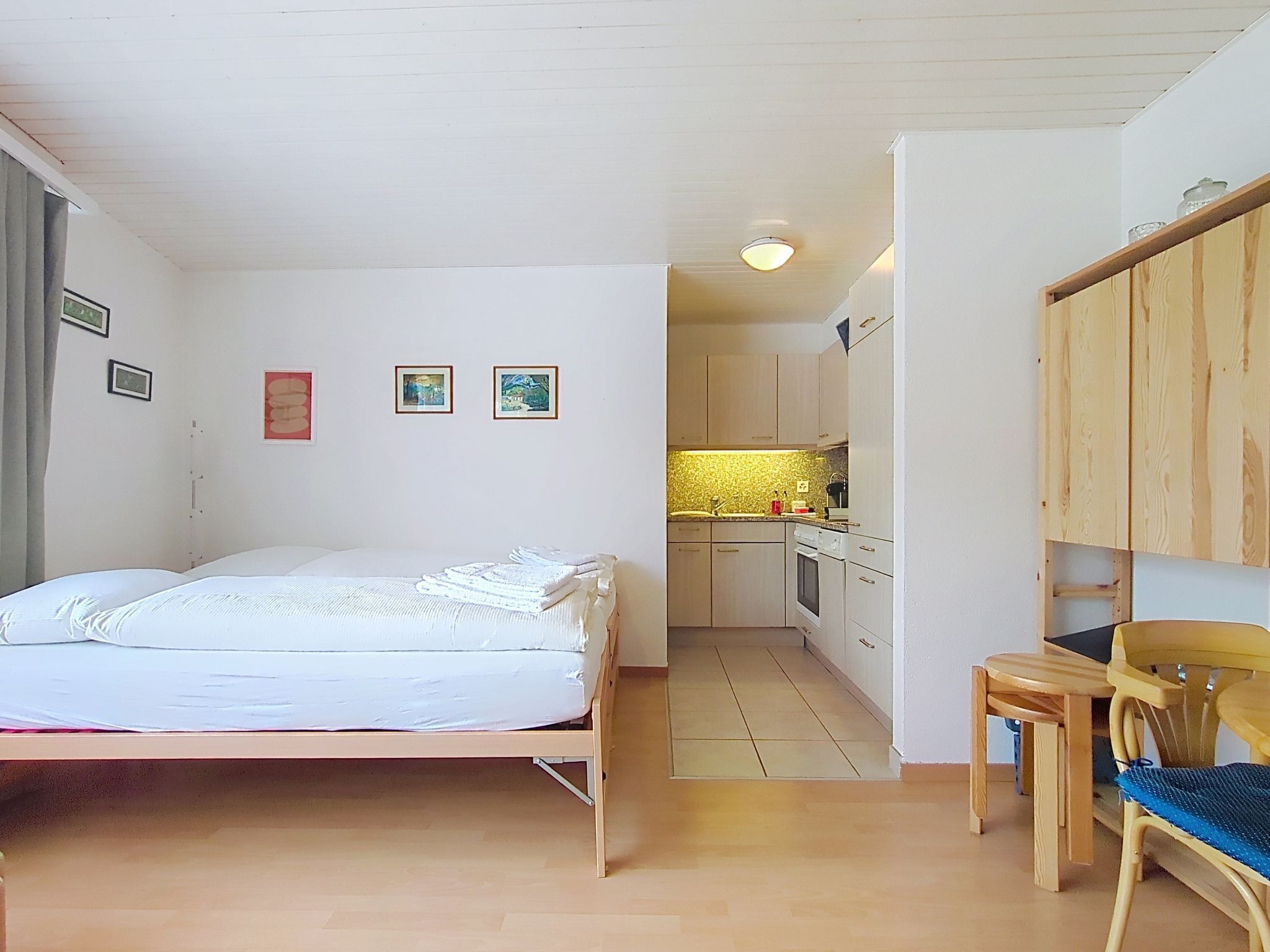 A bedroom with a bed, a small desk with a chair, a kitchenette with a sink and stove, and a bathroom with a toilet.