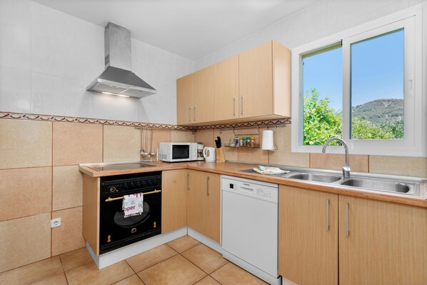 A kitchen with wooden cabinets, a microwave, a dishwasher, and a window with a view of greenery.