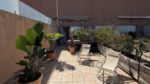 Eine Dachterrasse mit Topfpflanzen, Sitzgelegenheiten im Freien und einem Gebäude mit flachem Dach.