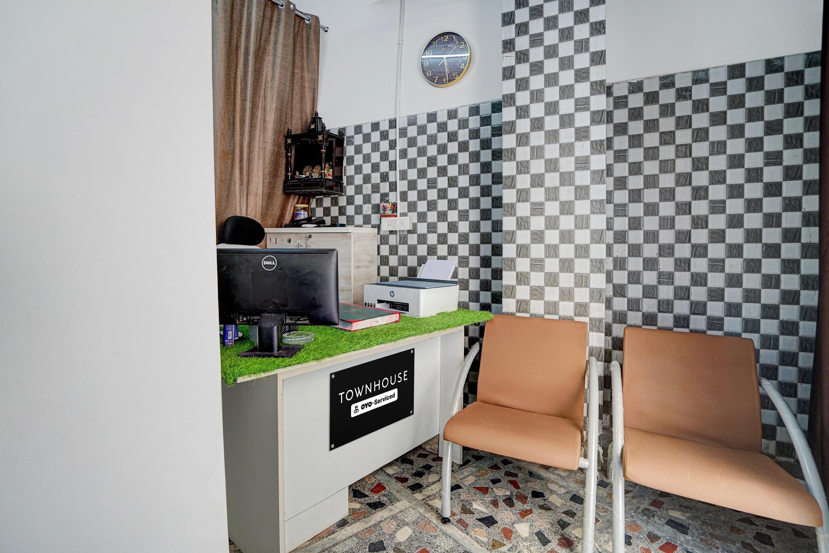 A reception area with a checkered wall, a clock, a desk with a computer, and a chair.