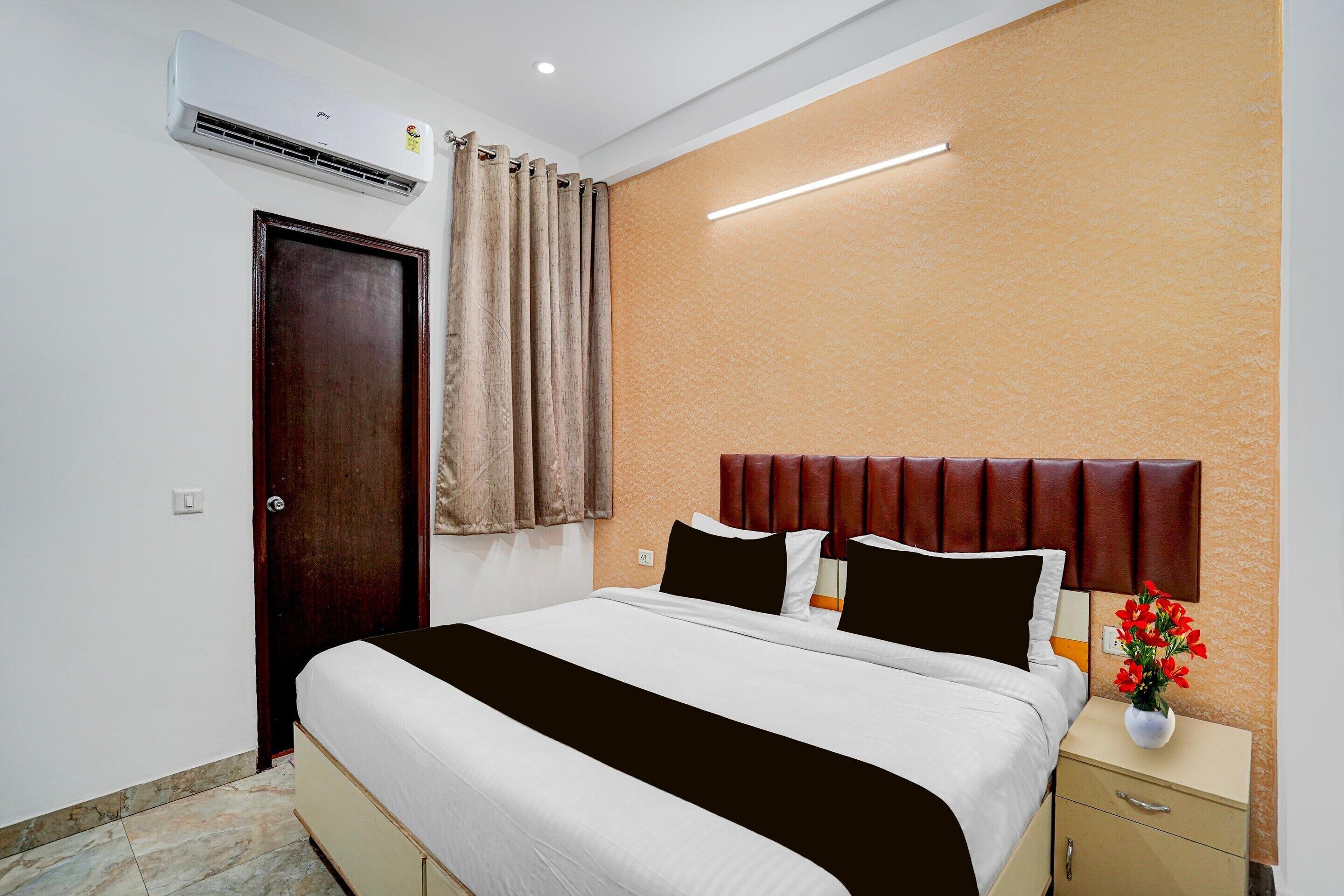Une chambre d’hôtel avec un lit, une table de chevet, un vase de fleurs, une porte en bois et un appareil de climatisation.