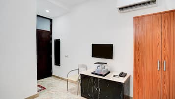A hotel room with a desk, a flat-screen TV, a telephone, a wooden wardrobe, and a door.