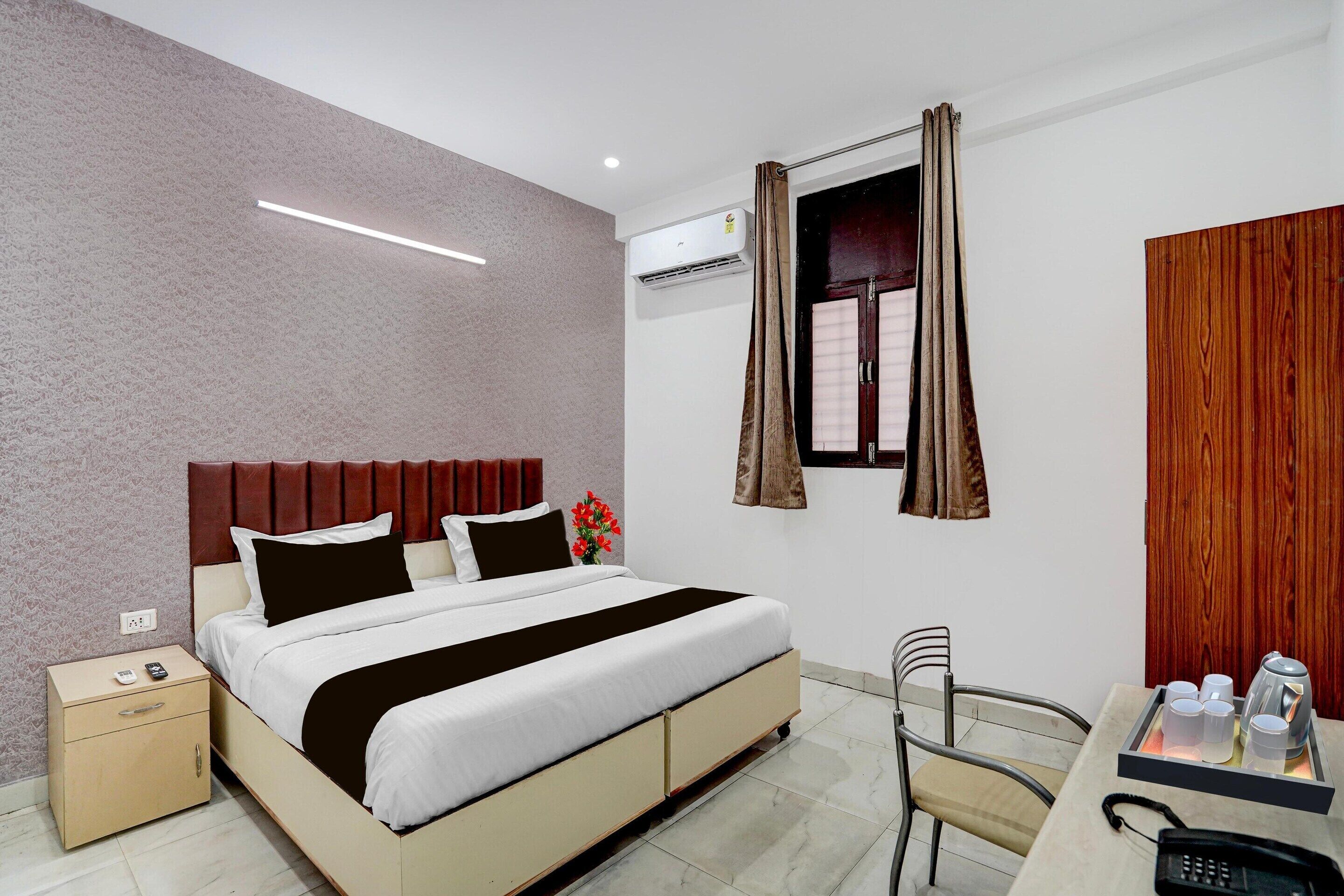 A hotel room with a bed, bedside table, chair, and a desk with a phone and cups.