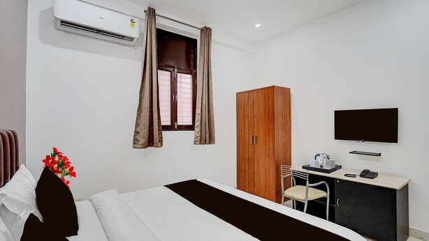 A hotel room with a bed, a desk with a chair, a wardrobe, a television, and an air conditioning unit. - Townhouse Sector 13 Gurgaon (Gurugram)