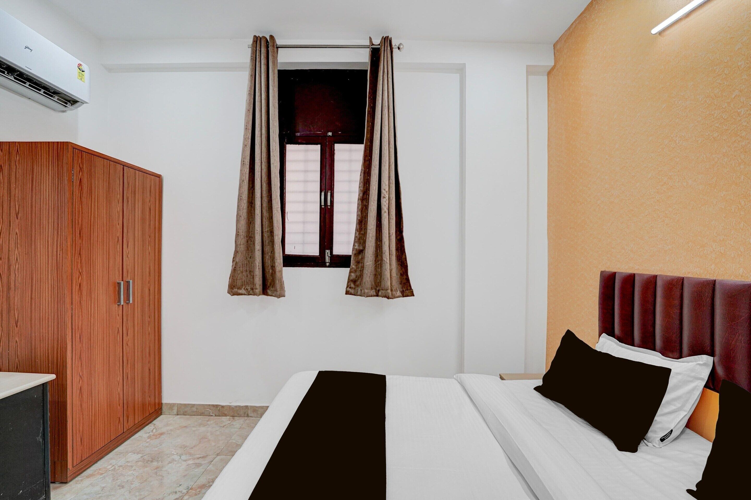 A hotel room with a bed, a wardrobe, a window with curtains, and an air conditioning unit.