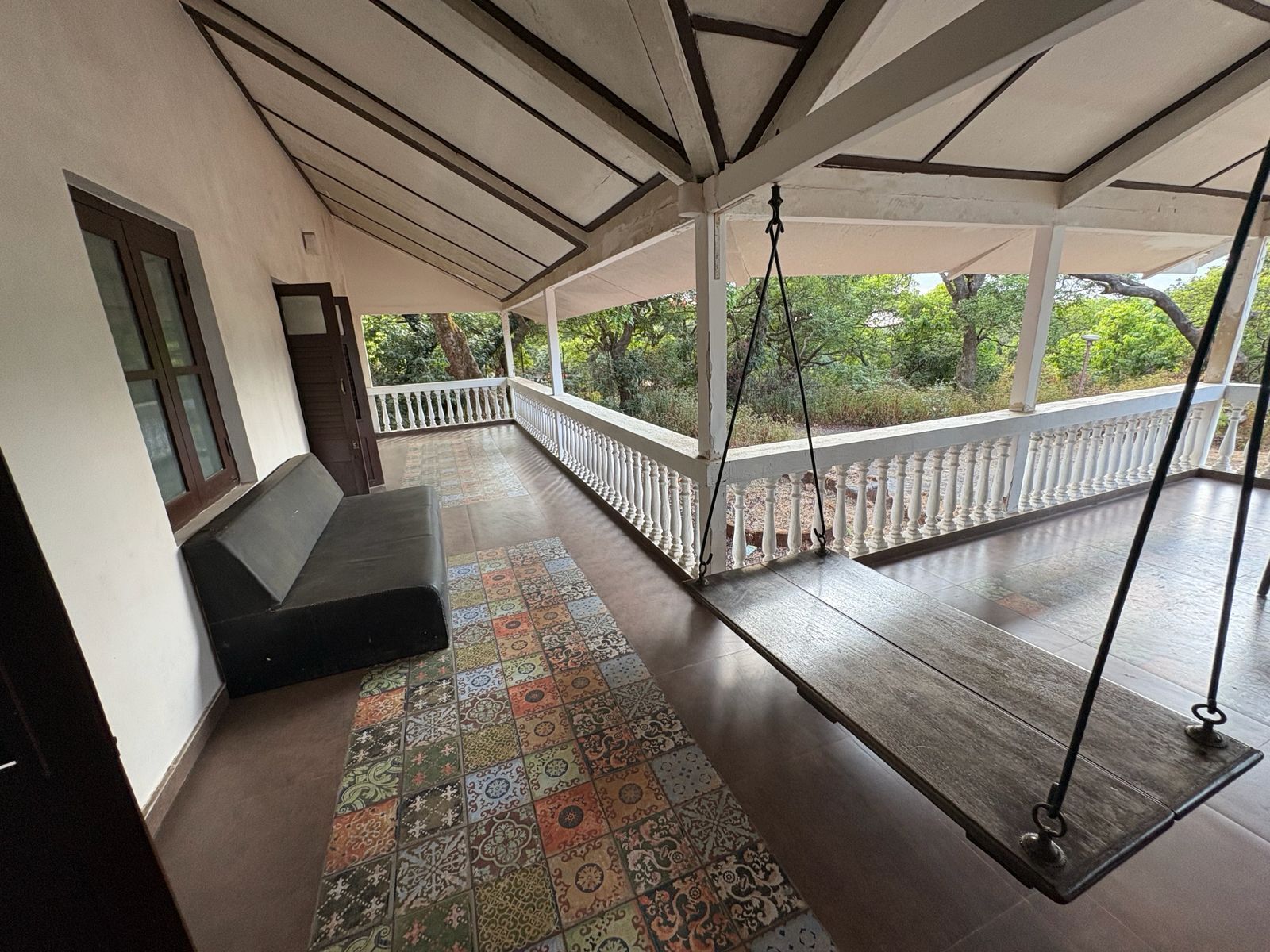 A covered porch with a bench, a swing, and a patterned floor.