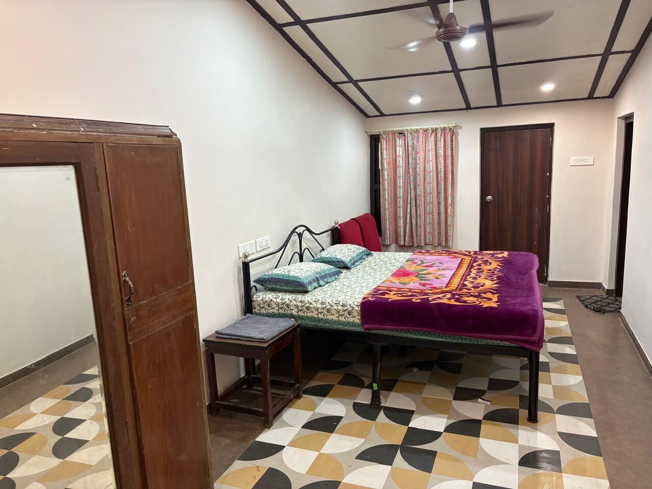 Une pièce comprenant un lit, une petite table, un ventilateur de plafond et un sol à motifs.