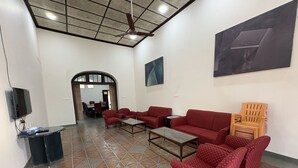 Amplia sala de estar con piso de baldosas, sofás rojos con estampado, una silla de madera, un televisor y un ventilador de techo.